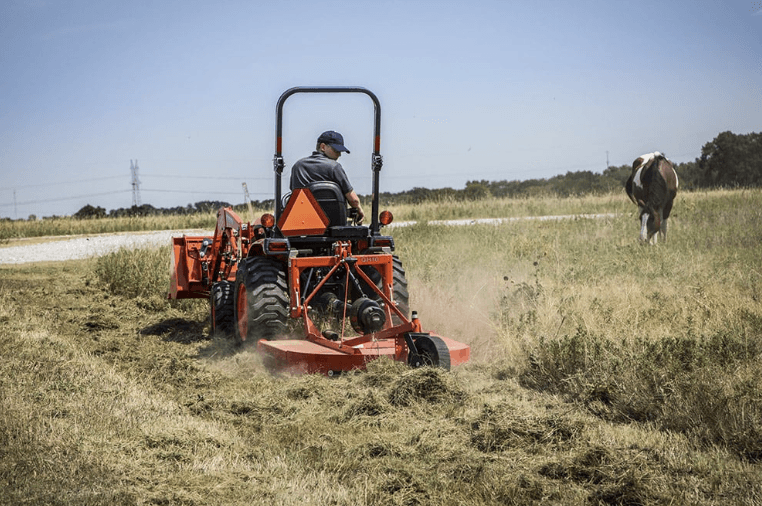 Man mowing field with rear mower implement